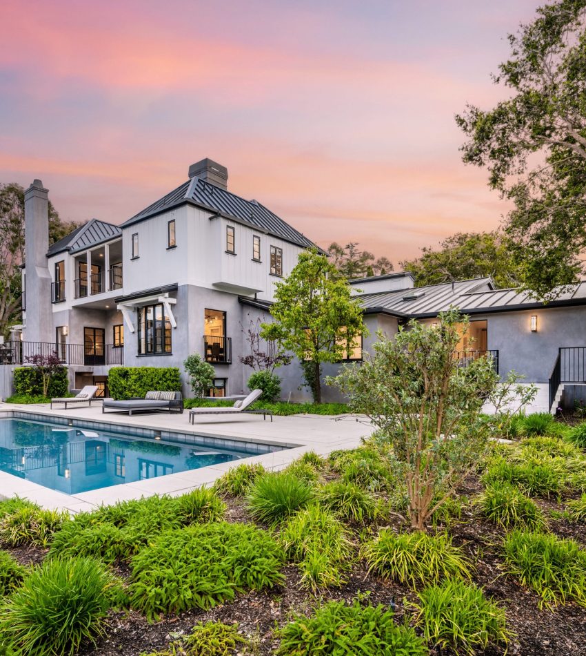 A stunning sunset view of a house with a pool in the foreground